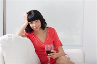 Young woman sitting on sofa with glass of wine. Photo: Dan Bannister