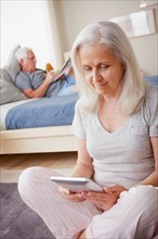 Senior woman holding photo frame, man sitting on bed in background. Photo: Rob Lewine