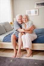 Senior couple sitting on bed in close embrace. Photo : Rob Lewine