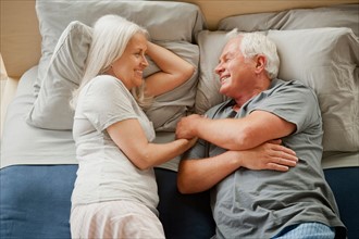 Senior couple laying on bed and laughing. Photo: Rob Lewine