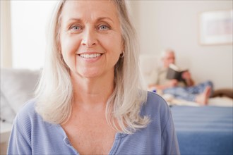 Senior woman smiling with husband reading in background. Photo : Rob Lewine