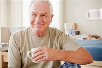 Senior man holding coffee cup and smiling. Photo : Rob Lewine