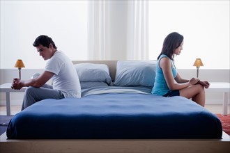 Mid adult couple after quarrel sitting on bed. Photo : Rob Lewine