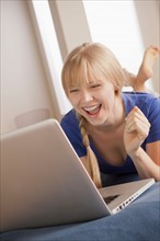 Laughing young woman lying on bed using laptop. Photo : Rob Lewine