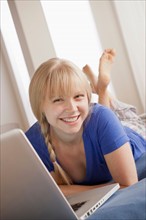 Portrait of smiling young woman lying on bed and using laptop. Photo : Rob Lewine