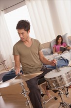 Man plying drums and woman reading in bed. Photo : Rob Lewine