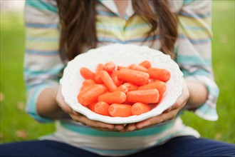 mid-section of mid adult woman holding bowl with carrots in focus. Photo: Jessica Peterson