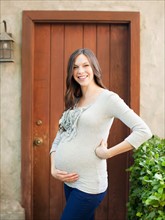 Portrait of pregnant mid adult woman standing in front of entrance door. Photo : Jessica Peterson