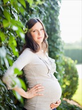 Portrait of pregnant mid adult woman next to hedge. Photo : Jessica Peterson