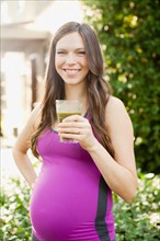 Portrait of pregnant mid adult woman in sport clothing holding glass with green juice. Photo: