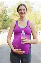 Front view portrait of pregnant mid adult woman in sport clothing holding water bottle. Photo :