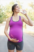 Front view of pregnant mid adult woman in sport clothing drinking water. Photo: Jessica Peterson