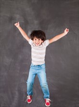 Studio portrait of boy (6-7) jumping in front of blackboard. Photo : Jessica Peterson