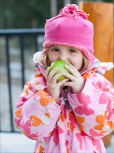 Girl (4-5) wearing warm clothing eating outdoors. Photo : Jessica Peterson