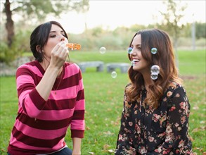 Two young women blowing bubbles in park. Photo: Jessica Peterson