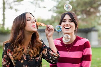 Two young women blowing bubbles in park. Photo : Jessica Peterson