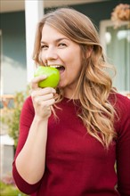 Portrait of young woman biting green apple. Photo: Jessica Peterson