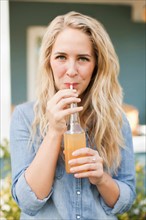 Front view portrait of young woman drinking soda through drinking straw. Photo: Jessica Peterson
