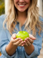 Mid-section of young woman holding green apple. Photo : Jessica Peterson