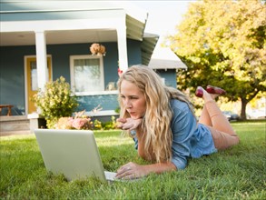 Young woman lying down on grass with her laptop, blowing a kiss. Photo: Jessica Peterson