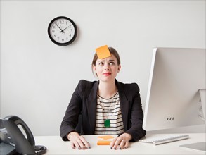 Studio shot of young woman working in office with adhesive note on her forehead. Photo: Jessica