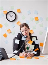 Studio shot of young woman working in office covered with adhesive notes. Photo: Jessica Peterson