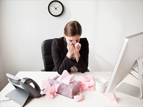 Studio shot of young woman working in office sneezing. Photo: Jessica Peterson