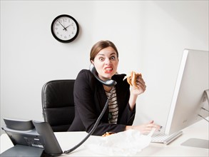 Studio shot of young woman working in office and having lunch same time. Photo: Jessica Peterson