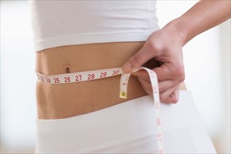 Midsection of woman measuring waistline.