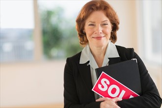 Portrait of female real estate agent holding sold sign.