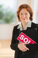 Portrait of female real estate agent holding sold sign.