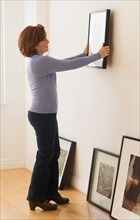 Woman hanging picture on wall.