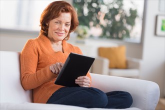 Woman sitting on sofa using digital tablet.