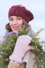 Portrait of young woman wearing knit hat, gloves and scarf an carrying fir wreath.