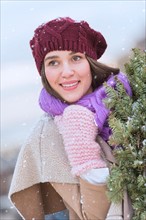 Portrait of young woman wearing knit hat, gloves and scarf an carrying fir wreath.