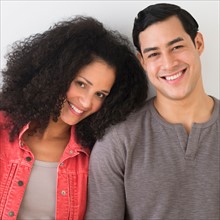 Portrait of smiling couple standing against white wall.