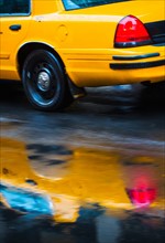 Yellow cab reflecting in rain puddle.