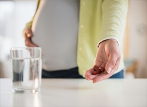 Pregnant woman holding medicine with glass of water in front