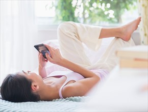 View of Teenage girl ( 16-17 years) using mobile phone lying on bed