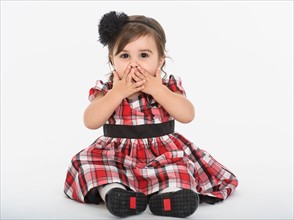 Portrait of Baby girl ( 6-11 months) wearing plaid dress with hands on mouth