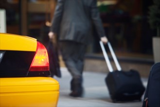 Rear view of businessman pulling suitcase by yellow taxi