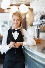Portrait of smiling waitress standing by bar counter