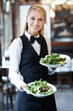 Portrait of young waitress holding plates with salad