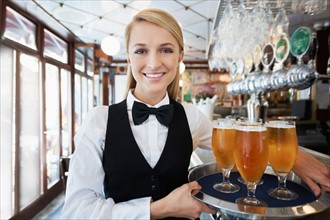 Portrait of young woman holding tray with beer glasses