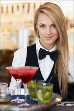 Portrait of female bartender holding tray with cocktails