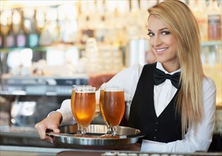 Portrait of young woman holding tray with beer glasses