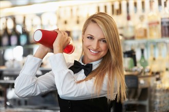 Young female bartender using cocktail shaker