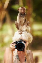 Portrait of female photographer with macaque monkey sitting atop her head