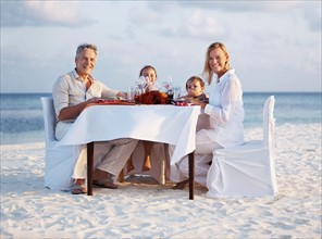Portrait of parents with daughters (8-9), (4-5) sitting at table on beach