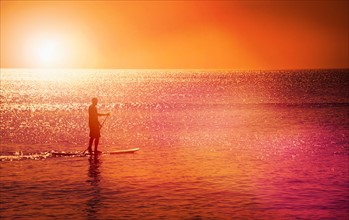 Man standing on paddle board at sunset